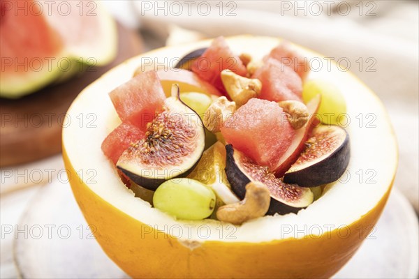 Vegetarian fruit salad of watermelon, grapes, figs, pear, orange, cashew on white wooden background and linen textile. Side view, close up, selective focus