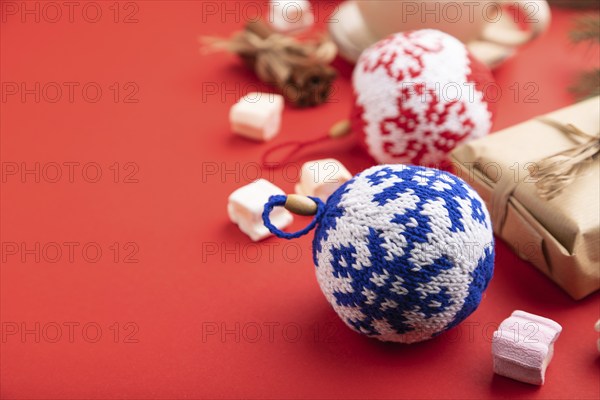 Christmas or New Year composition. Decorations, box, cinnamon, knitted balls, fir and spruce branches, cup of coffee, on a red paper background. Side view, copy space, selective focus