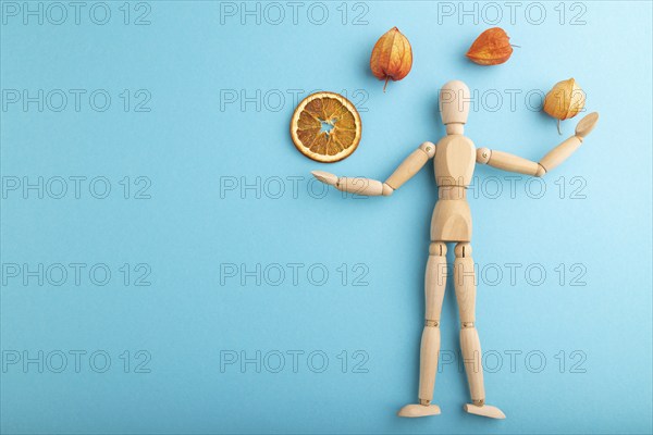 Wooden mannequin juggling dried citrus and physalis on blue pastel background. copy space, isolated