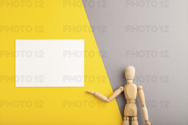 Wooden mannequin holding white blank poster on gray and yellow pastel background. copy space, isolated, presentation concept, trendy colors