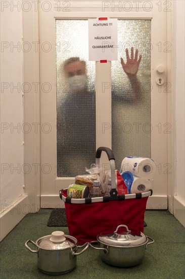 Symbolic image Domestic quarantine, man is in isolation at home due to a suspected corona infection, warning sign for visitors on the front door, communicates with a visitor through the door, neighbours have been shopping, cooked and put the things in front of the door