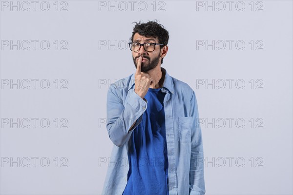 Pensive young man with finger on his lips on an isolated background. Worried guy with finger on his lips thinking isolated