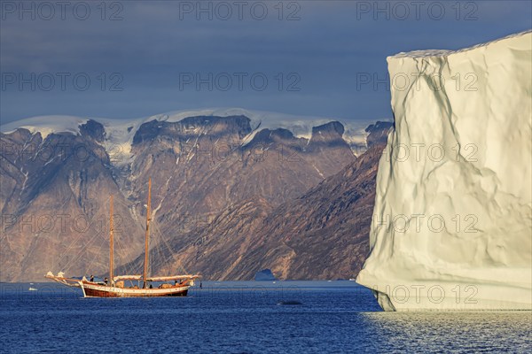 Sailing boat, ship in fjord in front of large icebergs and mountains, evening light, Scoresby Sound, East Greenland, Greenland, North America