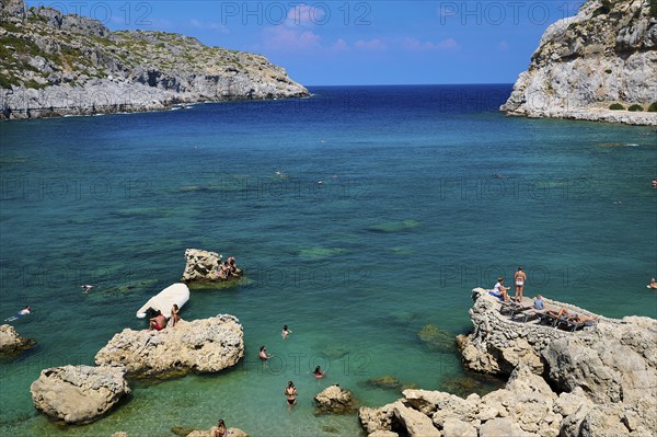 Sunbathing people on rocks on a coast with deep blue water and sunny sky, Anthony Quinn Bay, Vagies Bay, Rhodes, Dodecanese, Greek Islands, Greece, Europe