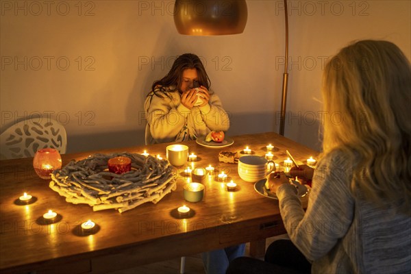 Symbolic image energy saving, cold winter, energy crisis, cold flat, mother and daughter dressed warmly at dinner, only by candlelight, heating on to a minimum