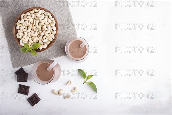 Organic non dairy cashew chocolate milk in glass and wooden plate with cashew nuts on a gray concrete background. Vegan healthy food concept, flat lay, top view, copy space