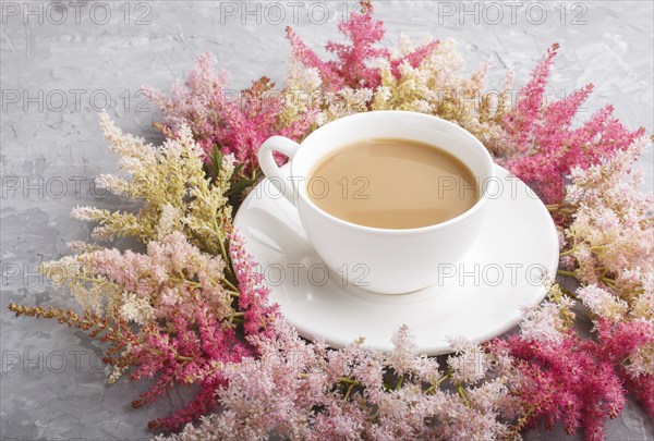 Pink and red astilbe flowers and a cup of coffee on a gray concrete background. Morninig, spring, fashion composition. side view, close up