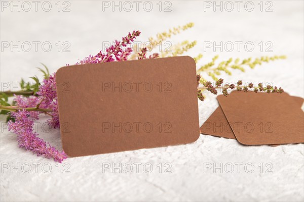 Brown paper business card mockup with purple astilbe flowers on gray concrete background. Blank, side view, copy space, still life. spring concept