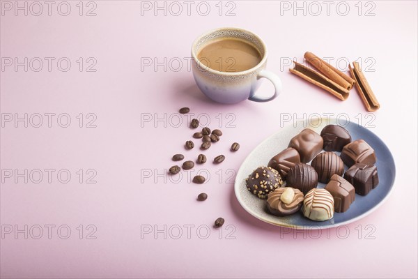 Different chocolate candies and a cup of coffee on a pink pastel background. side view, copy space