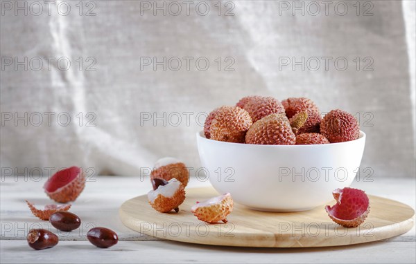 Lychee in a white plate on a white wooden background, close up