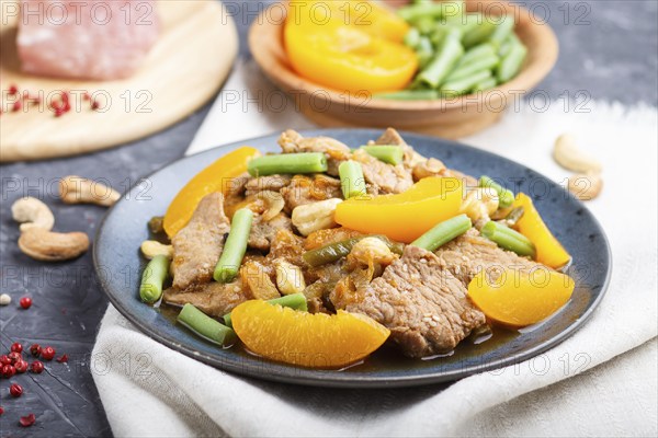 Fried pork with peaches, cashew and green beans on a black concrete background. Side view, close up, chinese cuisine, selective focus, macro