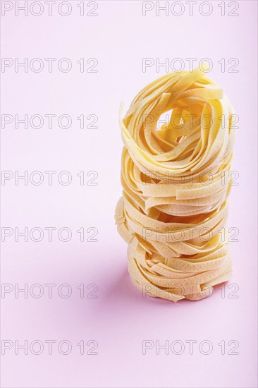 Raw uncooked tagliatelle pasta on a pink pastel background. side view, close up, copy space