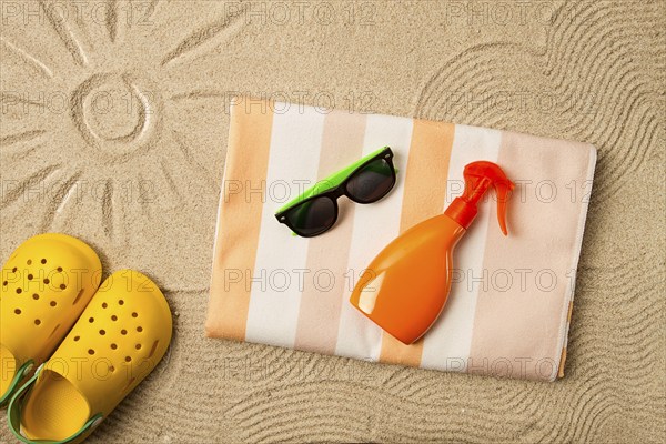 Drawing on the sand, sun and waves, sunglasses, with an orange bottle, yellow rubber slippers, beach towel, sun spray, on the sand, top view, no people