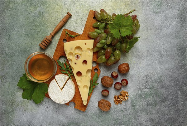 Cheese with big holes, emmental, maasdam, brie cheese, on a cutting board, with grapes and honey, nuts, appetizer to wine, top view