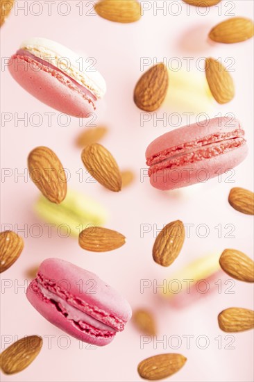 Multicolored flying macaroons and almonds frozen in the air on blurred pink background. top view, flat lay, close up. Breakfast, morning, concept