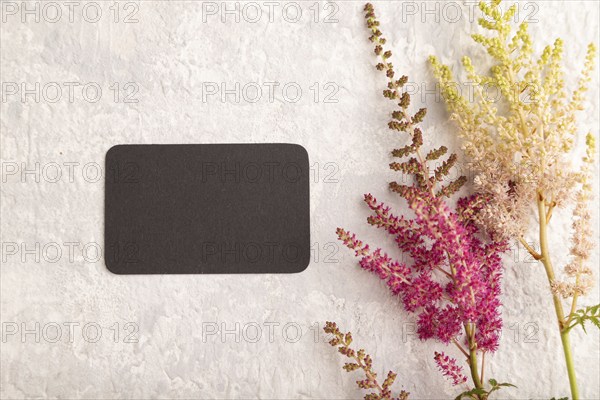 Black paper business card mockup with purple astilbe flowers on gray concrete background. Blank, top view, copy space, still life. spring concept