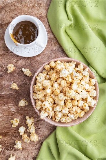 Popcorn with caramel in ceramic bowl on brown concrete background and green textile. Top view, flat lay, close up