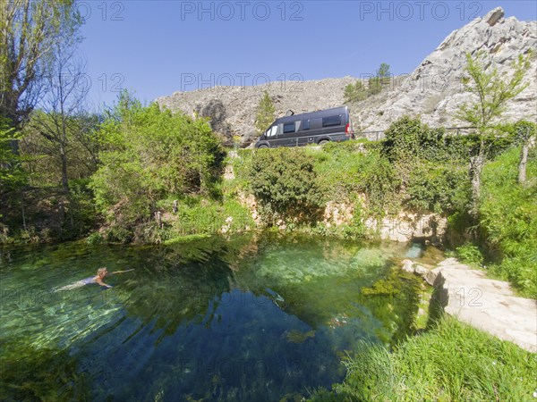 Eine Person schwimmt in einer klaren Quelle in den Bergen neben einem parkenden Van an einem sonnigen Tag, Wohnmobil, natürliche warme Quelle, Fuente de la Salud, am Fluss Duratón, Sepúlveda, Sepulveda, Segovia, Kastilien und León, Spanien