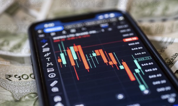 Stock market graph or chart display on a mobile phone against Indian 500 rupee paper currency note