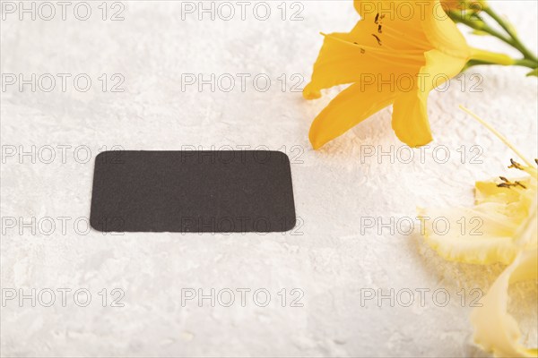 Black paper business card mockup with orange day-lily flower on gray concrete background. Blank, side view, copy space, still life. spring concept