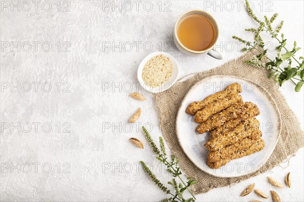 Crumble cookies with seasme and almonds on ceramic plate with cup of green tea and linen textile on gray concrete background. top view, flat lay, copy space