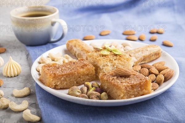 Traditional arabic sweets (basbus, kunafa, baklava), a cup of coffee and nuts on a gray concrete background and blue textile. side view, close up, selective focus