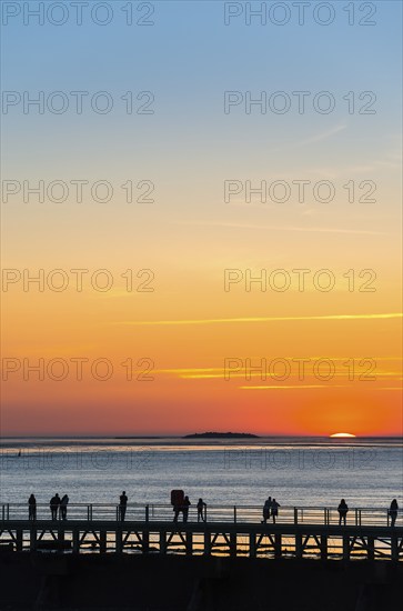 Silhouettes of several people on the pier free canal, couple and single persons watch from a jetty the picturesque, golden, breathtakingly beautiful sunset over the sea, island Langlütjen II far away on the horizon, sun almost completely sunk, crescent, orange and blue glowing cloudless sky, wide sea in soft colours, calm atmosphere, mouth of the Weser into the North Sea, Outer Weser, Bremerhaven, Land Bremen, Germany, Europe