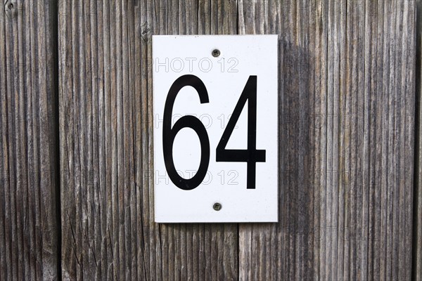 64, number, sixty-four, sign, The numbers 6 and 4 are written in black numbers on a white sign. The sign is attached to a wooden fence