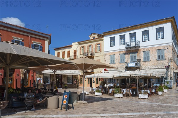 Lively street café with large parasols and colourful buildings under a blue sky, Syntagma Square, Nafplio, Nauplia, Nafplion, Nafplion, Argolis, Peloponnese, Greece, Europe