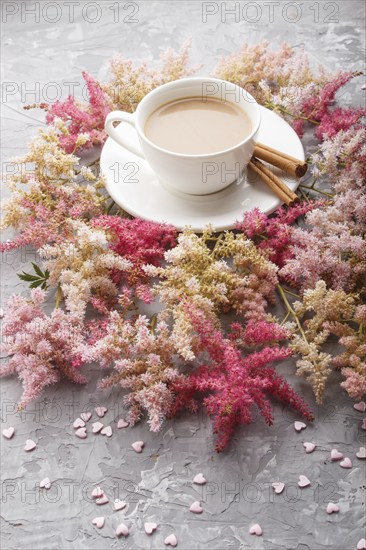 Pink and red astilbe flowers and a cup of coffee on a gray concrete background. Morninig, spring, fashion composition. side view, close up