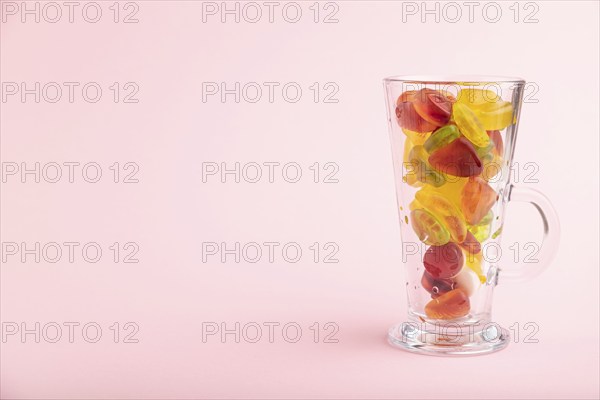 Various fruit jelly candies in drinking glass on pink pastel background. side view, copy space