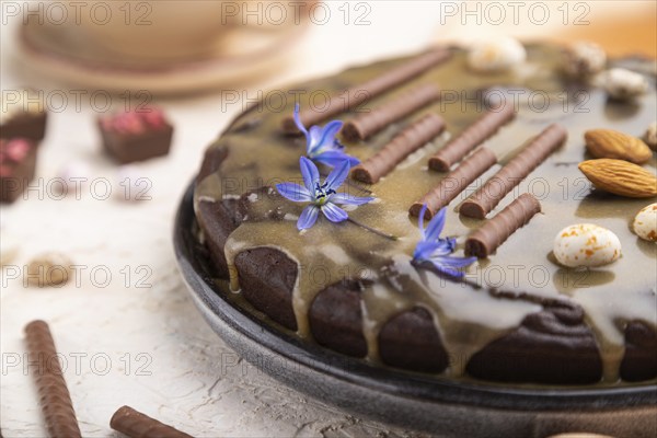 Homemade chocolate brownie cake with caramel cream and almonds with cup of coffee on a white concrete background and orange textile. Side view, close up, selective focus