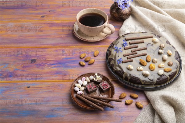 Homemade chocolate brownie cake with caramel cream and almonds with cup of coffee on a colored wooden background and linen textile. Side view, copy space