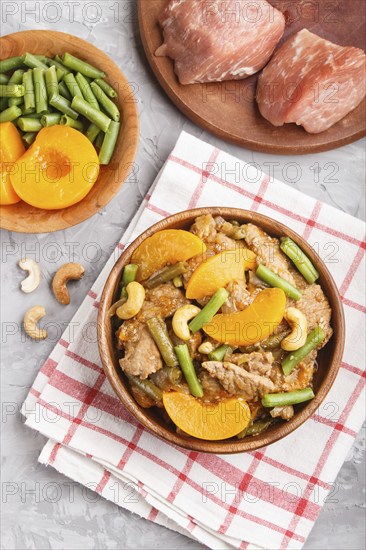 Fried pork with peaches, cashew and green beans on a black concrete background. top view, close up, flat lay, chinese cuisine. linen textile