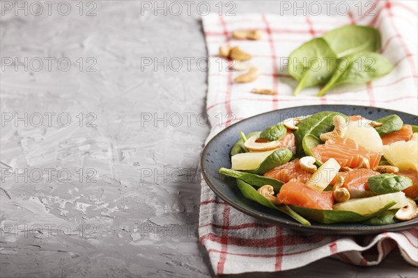 Fresh salmon with pineapple, spinach and cashew on a gray concrete background. Side view, copy space, linen tablecloth