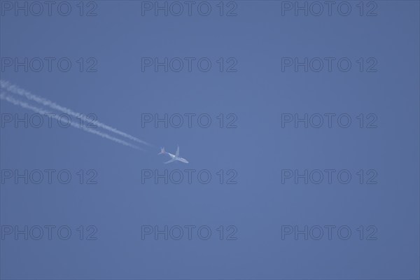 Jet aircraft in flight with a contrail or vapour trail across a blue sky, England, United Kingdom, Europe