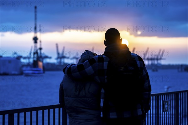 Port of Hamburg, couple looking at the Blohm + Voss shipyard, evening, cranes of the container terminals, sunset, Hamburg Germany