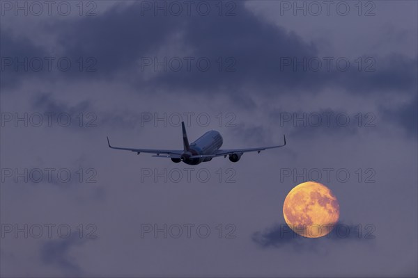 An aeroplane flies through the cloudy sky at night in front of a large, shining full moon, super moon, Stuttgart, Baden-Württemberg, Germany, Europe