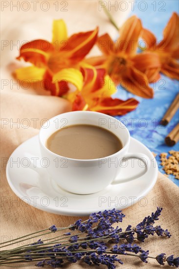 Orange day-lily and lavender flowers and a cup of coffee on a blue concrete background, with orange textile. Morninig, spring, fashion composition. side view, selective focus