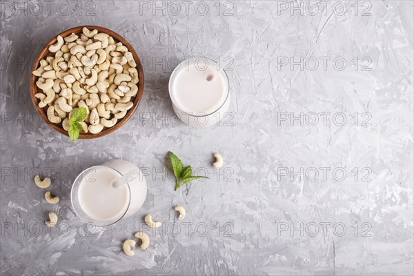 Organic non dairy cashew milk in glass and wooden plate with cashew nuts on a gray concrete background. Vegan healthy food concept, flat lay, top view, copy space