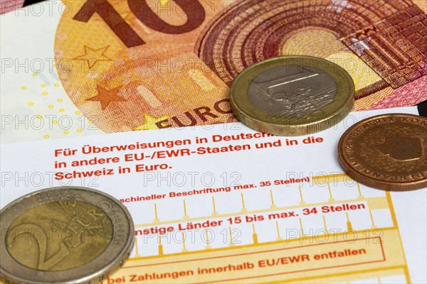 Symbolic image of payment transactions: close-up of a transfer form with euro coins and euro notes