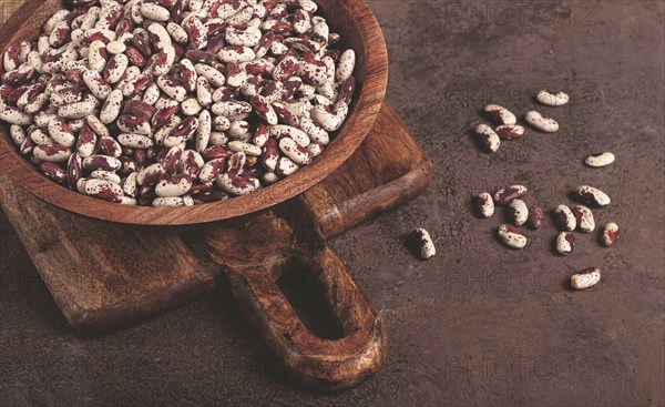 Variegated beans, red with white spots, raw in a wooden bowl, top view, no people