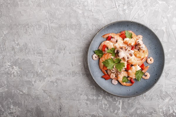 Boiled shrimps or prawns and small octopuses with herbs on a blue ceramic plate on a gray concrete background. Top view, flat lay, copy space