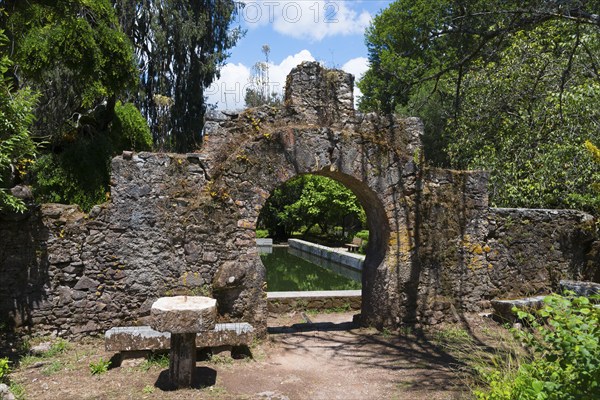 Ein alter Steinbogen führt in einen grünen Garten an einem sonnigen Tag, Mata Nacional do Buçaco, National-Wald von Bussaco, Bucaco, Mealhada, Beira Litoral, Portugal, Europe