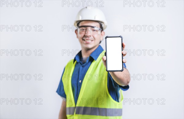 Smiling engineer showing cell phone screen isolated. Young construction engineer showing an advertisement on the phone screen