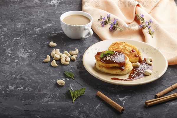 Cheese pancakes with caramel sauce on a beige ceramic plate and a cup of coffee on a black concrete background. side view, copy space, close up