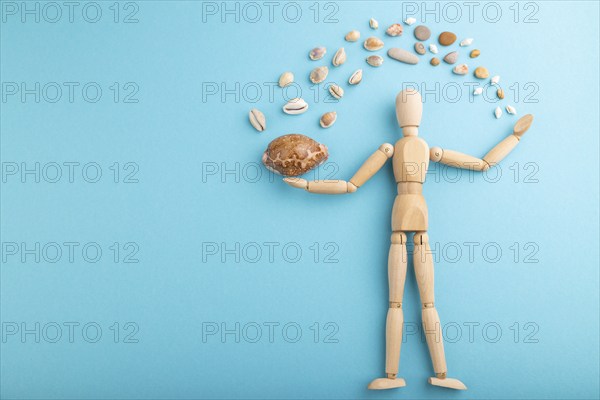 Wooden mannequin juggling sea shells on blue pastel background. copy space, isolated, travel, vacation, summer concept