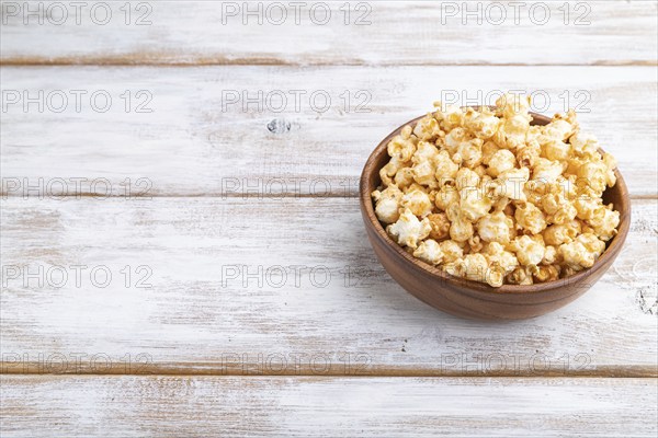 Popcorn with caramel in wooden bowl on a white wooden background. Side view, copy space