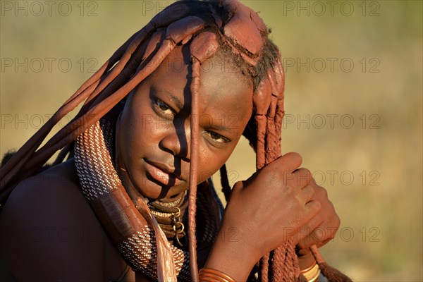 Young Himba woman doing her hair, Ombombo, Kaokoland, Kunene, Namibia, Africa