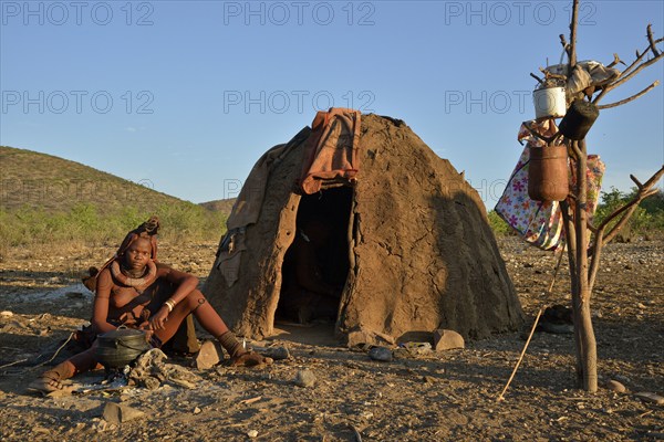 Young Himba woman sitting at a campfire in front of her hut, Ombombo, Kaokoland, Kunene, Namibia, Africa